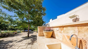 A patio area with a stone floor, a potted plant, a wall-mounted light fixture, and a built-in sink. - Mirto - Residenza Arcangela con Piscine nel Salento (Corsano)