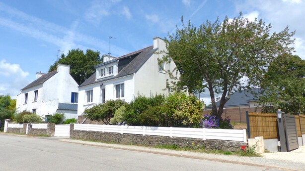 Une maison à deux étages, avec une façade blanche, un mur en pierre et une clôture en bois.