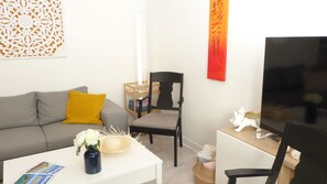 A living room with a grey sofa, a yellow pillow, a white vase with flowers, a white coffee table, a black chair, a TV, and a red abstract painting.