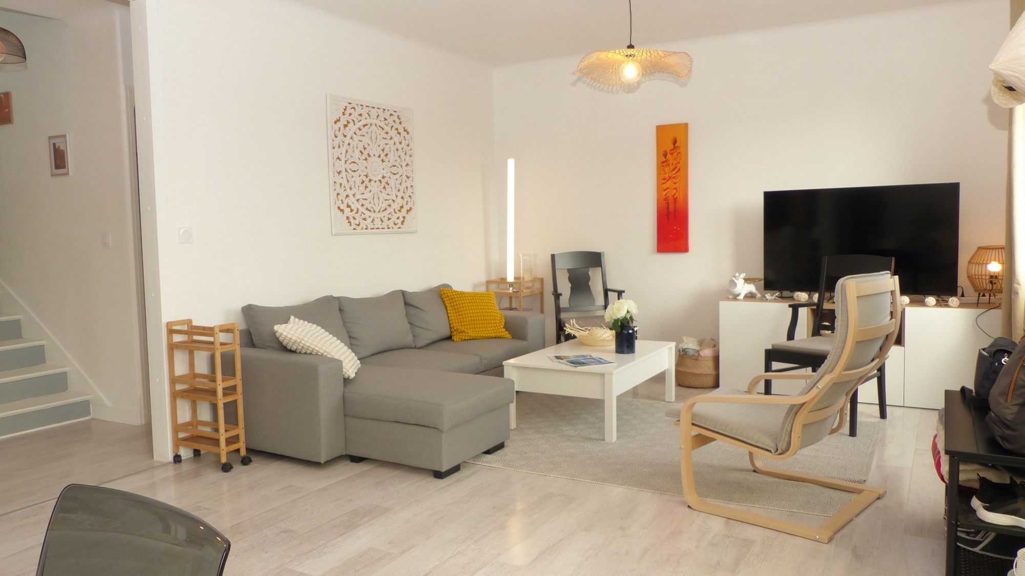 Un salon moderne avec un canapé gris, une table basse, un téléviseur et un fauteuil.