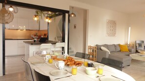 A modern kitchen with white cabinets, a dining table set for breakfast, and a living area with a sofa and a coffee table.
