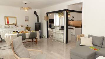 Un salon moderne avec un canapé gris, un coin repas avec une table mise pour le petit-déjeuner, et une cuisine visible à travers une porte ouverte.