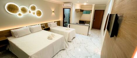 Habitación de hotel con dos camas, una kitchenette pequeña y un baño visible a través de una puerta abierta.