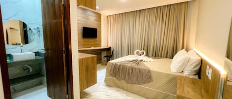 Une chambre d’hôtel moderne avec une salle de bain en marbre, un bureau, un lit décoré d’un motif en forme de cœur et un téléviseur fixé au mur.