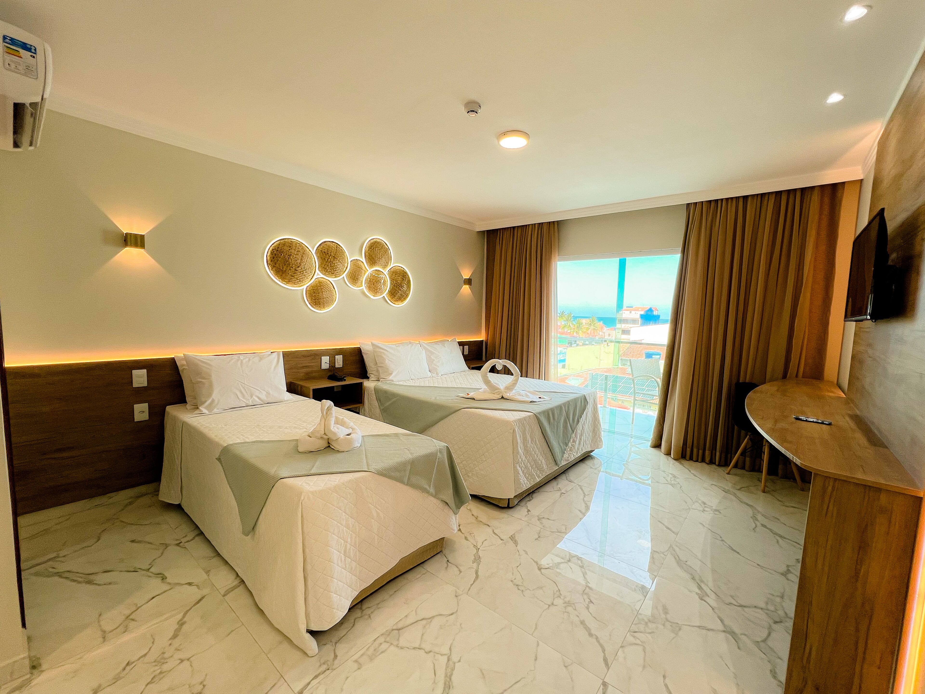 A hotel room with two beds, a small table, a TV, and a view of the ocean.