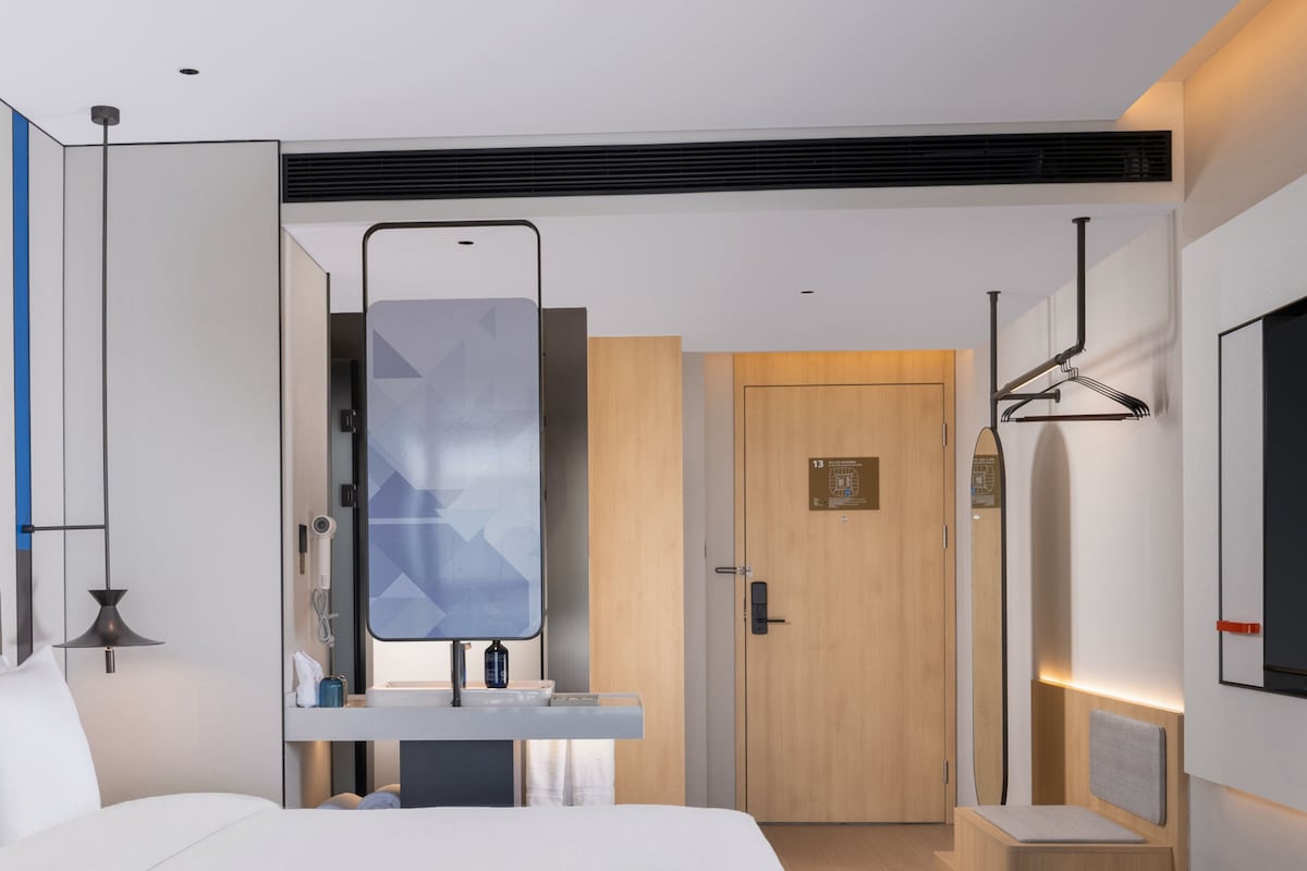 Una habitación de hotel moderna con una cama grande, una mesita de noche, un espejo, una puerta de madera y un televisor instalado en la pared.