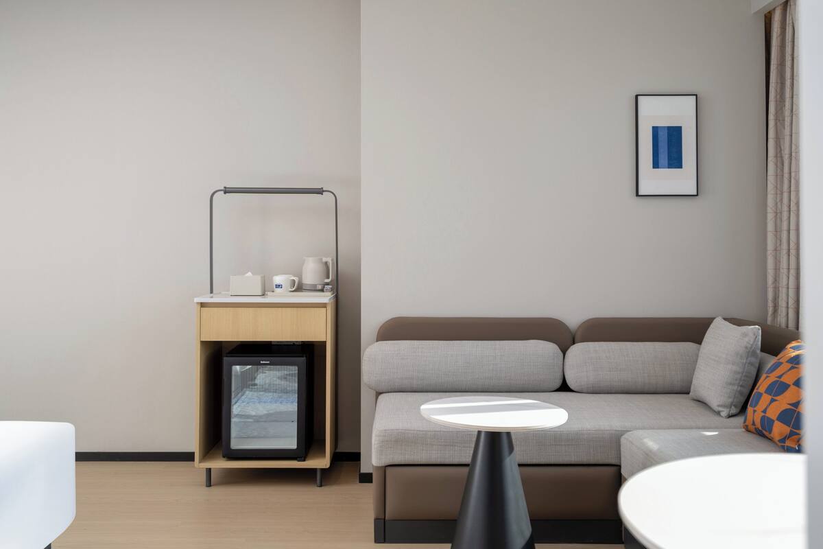 Une chambre d’hôtel moderne, équipée d’un canapé, d’une petite table, d’un minibar et d’un tableau encadré au mur.