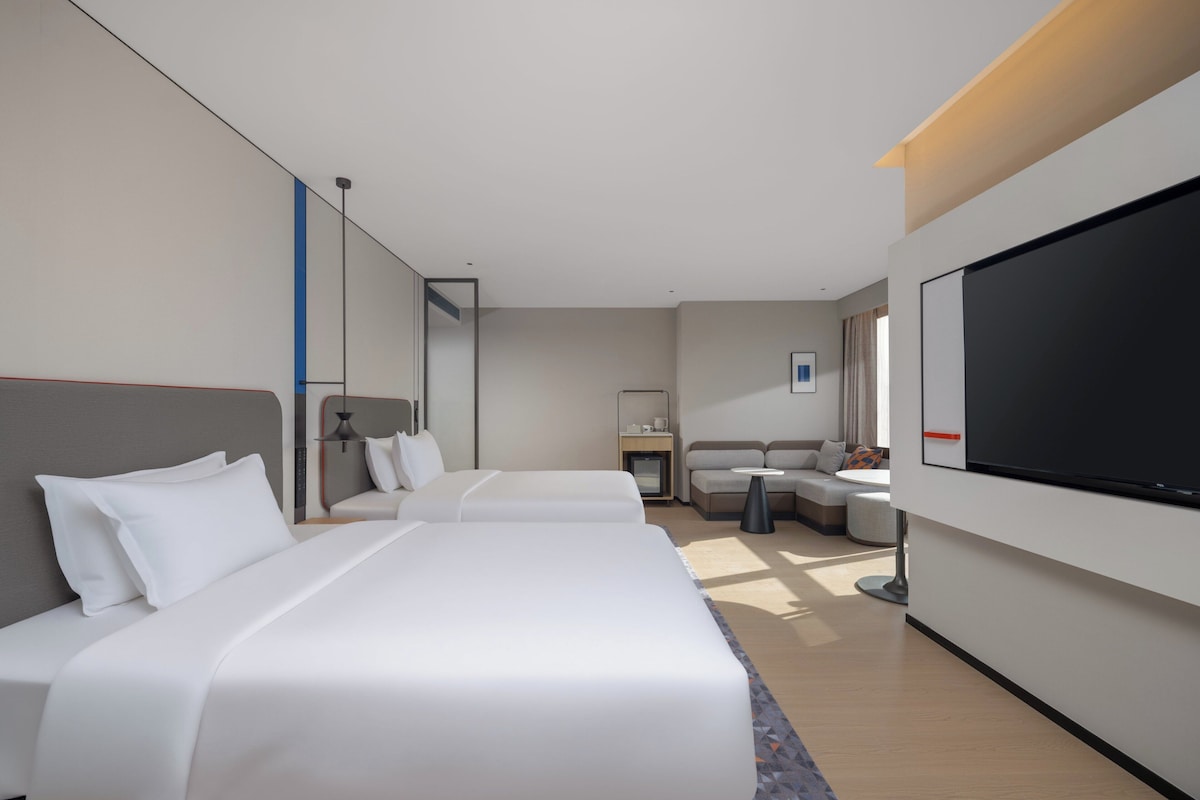 Una habitación de hotel moderna con dos camas, un sofá, un televisor y un escritorio con lámpara.