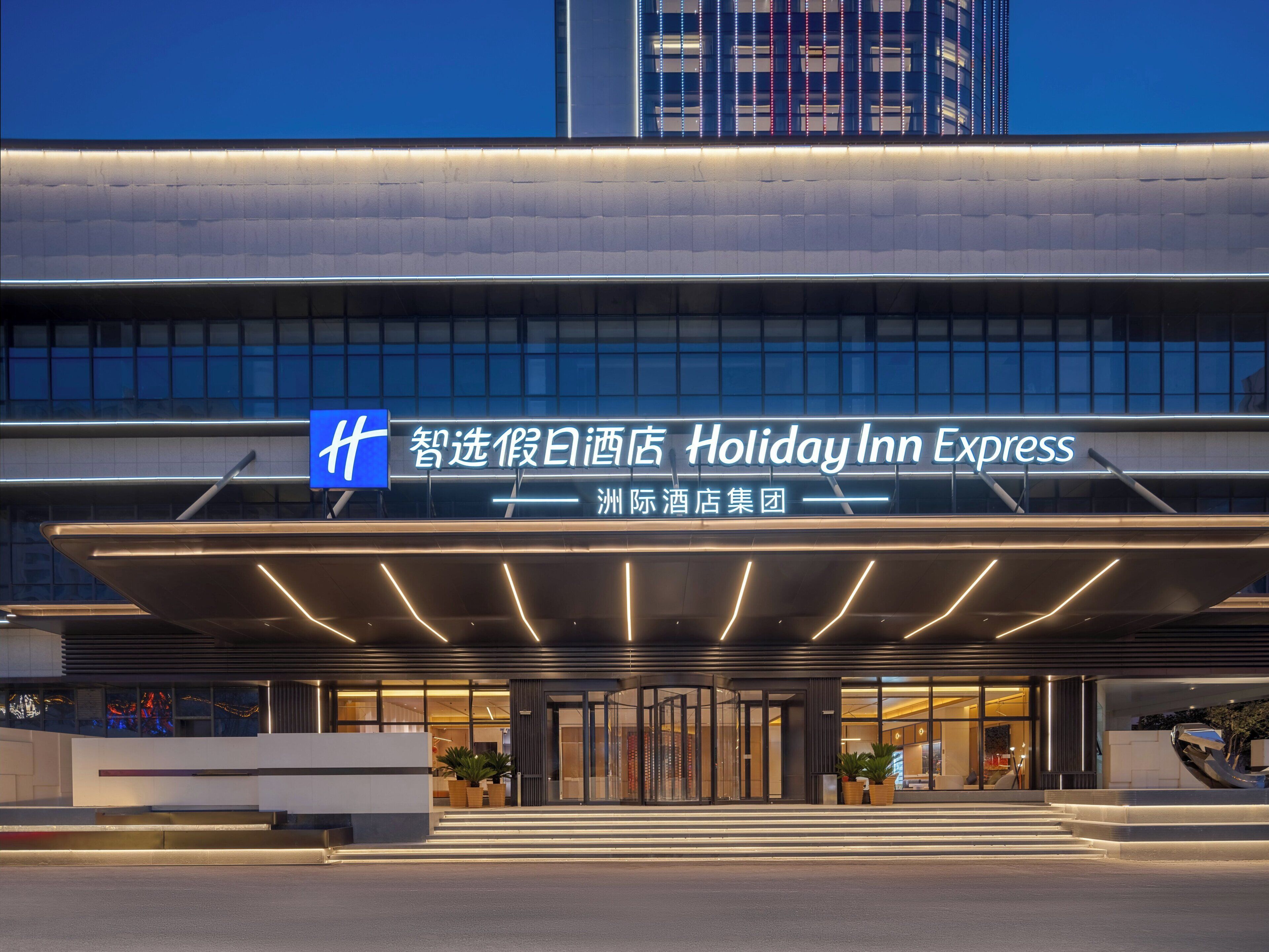 A Holiday Inn Express hotel entrance with a modern design, featuring a large sign, a covered entrance, and a staircase leading up to the lobby.