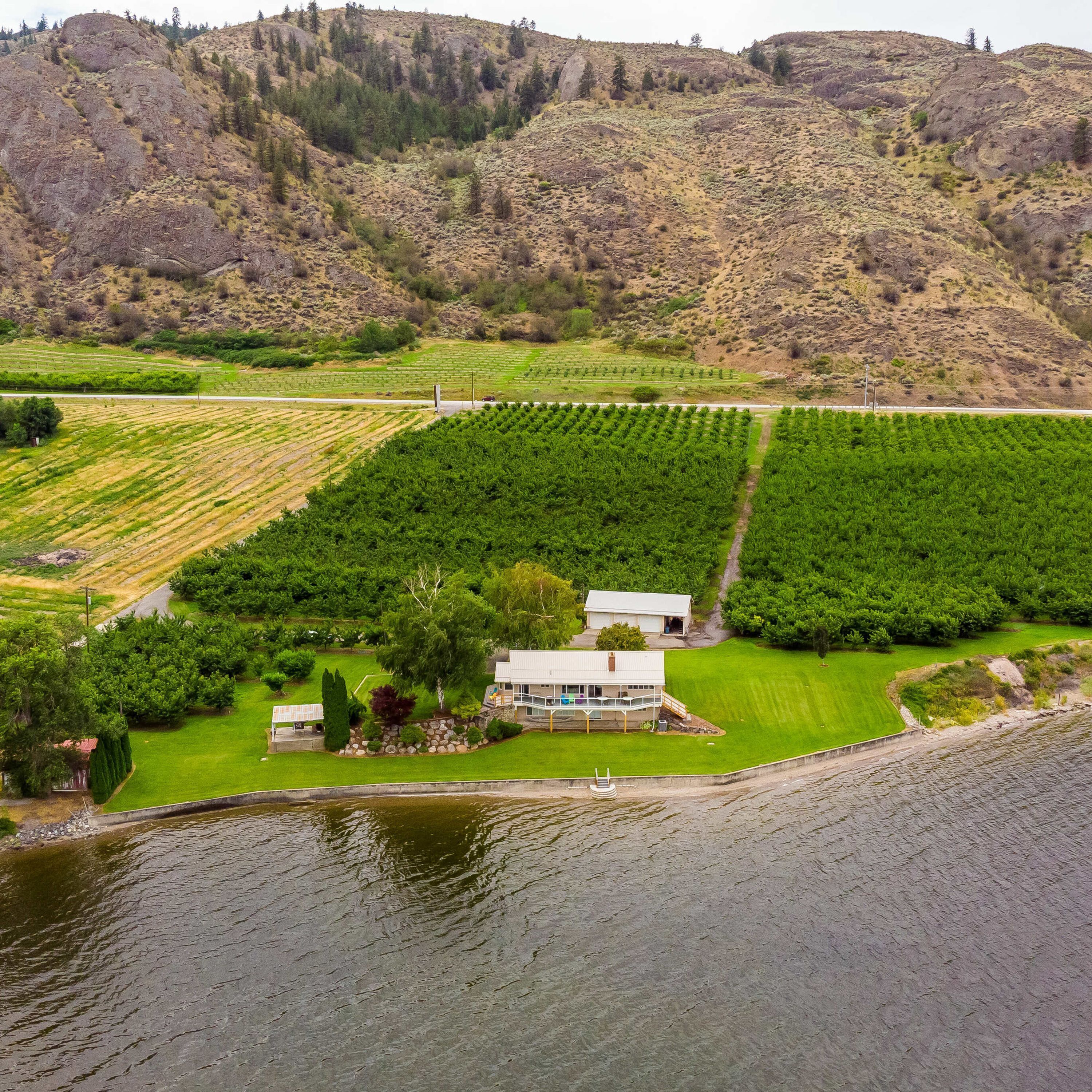 A house with a large lawn and a dock extending into a lake, surrounded by terraced fields.