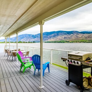 A covered deck with outdoor furniture and a grill, overlooking a lake with mountains in the background. - Linger Longer Lakeside Cottage (Oroville)