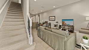 Ein modernes Wohnzimmer mit Treppe, einem großen Sofa, einem Fernseher und einem Essbereich.