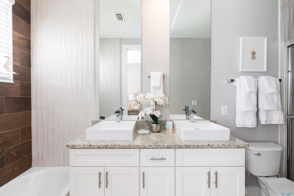 A modern bathroom with two sinks, a large mirror, white cabinets, and a toilet.