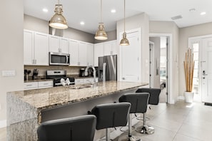 A modern kitchen with granite countertops, stainless steel appliances, and black bar stools.