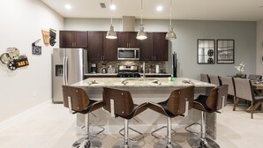 A modern kitchen with dark wooden cabinets, stainless steel appliances, and a central island with bar stools. - 5 BR 6 BA Villa 5min Disneyworld 2169ft (Kissimmee)