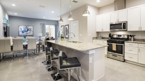 A modern kitchen with white cabinets, stainless steel appliances, and a central island with bar stools. - 4 BR 4 BA Villa 5min Disneyworld 1804ft BBQ (Kissimmee)