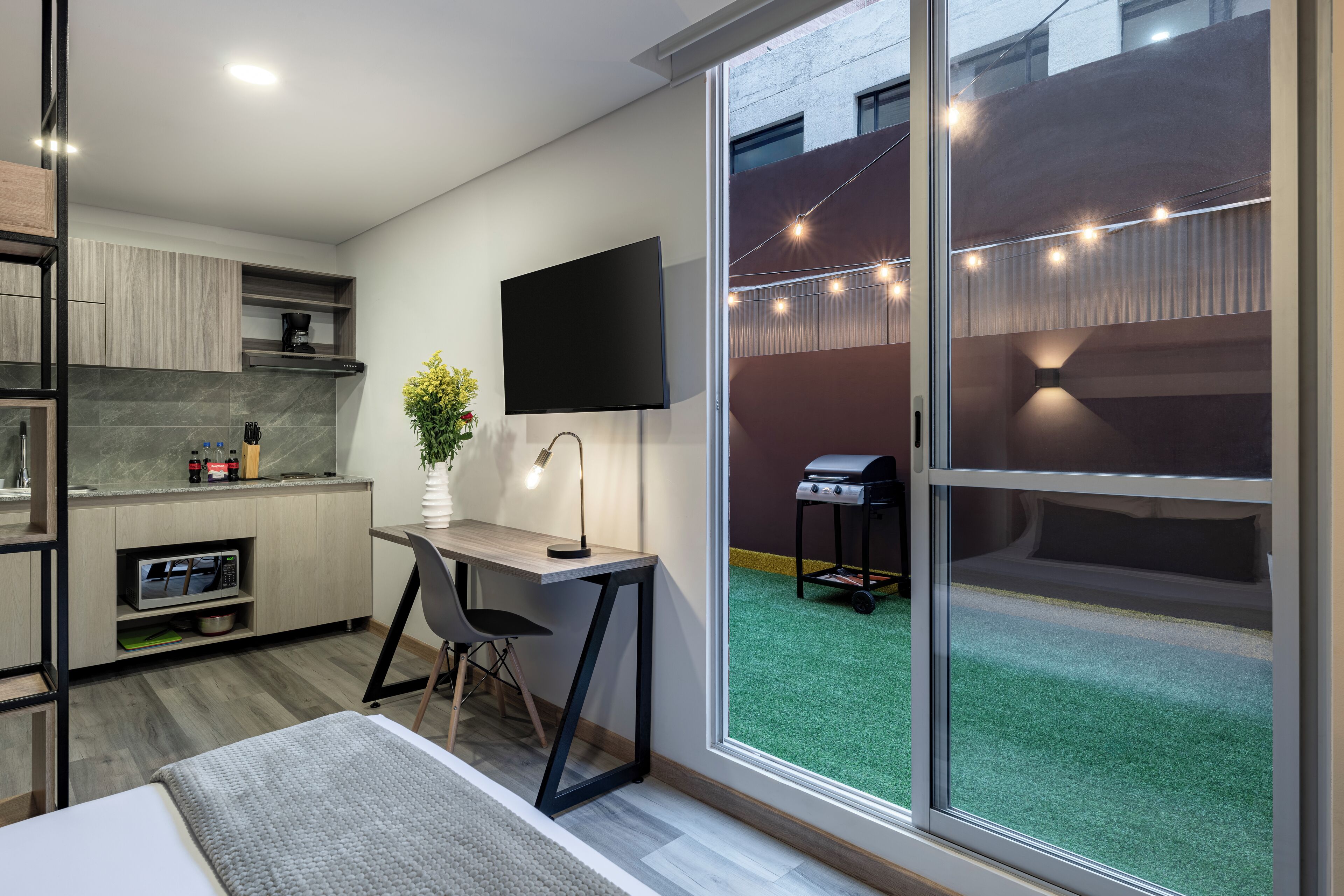 Una cocina moderna con una televisión de pantalla plana, un comedor con mesa y sillas, y un ventanal corredizo que da a un patio trasero con una parrilla.