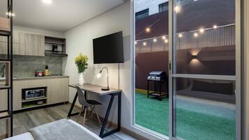 Una cocina moderna con una televisión de pantalla plana, un comedor con mesa y sillas, y un ventanal corredizo que da a un patio trasero con una parrilla.