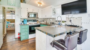 Une cuisine moderne avec des meubles blancs, un grand îlot central doté de tabourets, un four à micro-ondes et un téléviseur à écran plat fixé au-dessus de l’îlot.