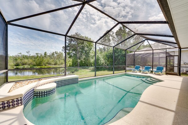 A covered swimming pool with a view of a lake and trees, surrounded by a metal frame structure. - Kissimmee Home w/ Pool + Pond View, 5 Mi to Disney (Kissimmee)