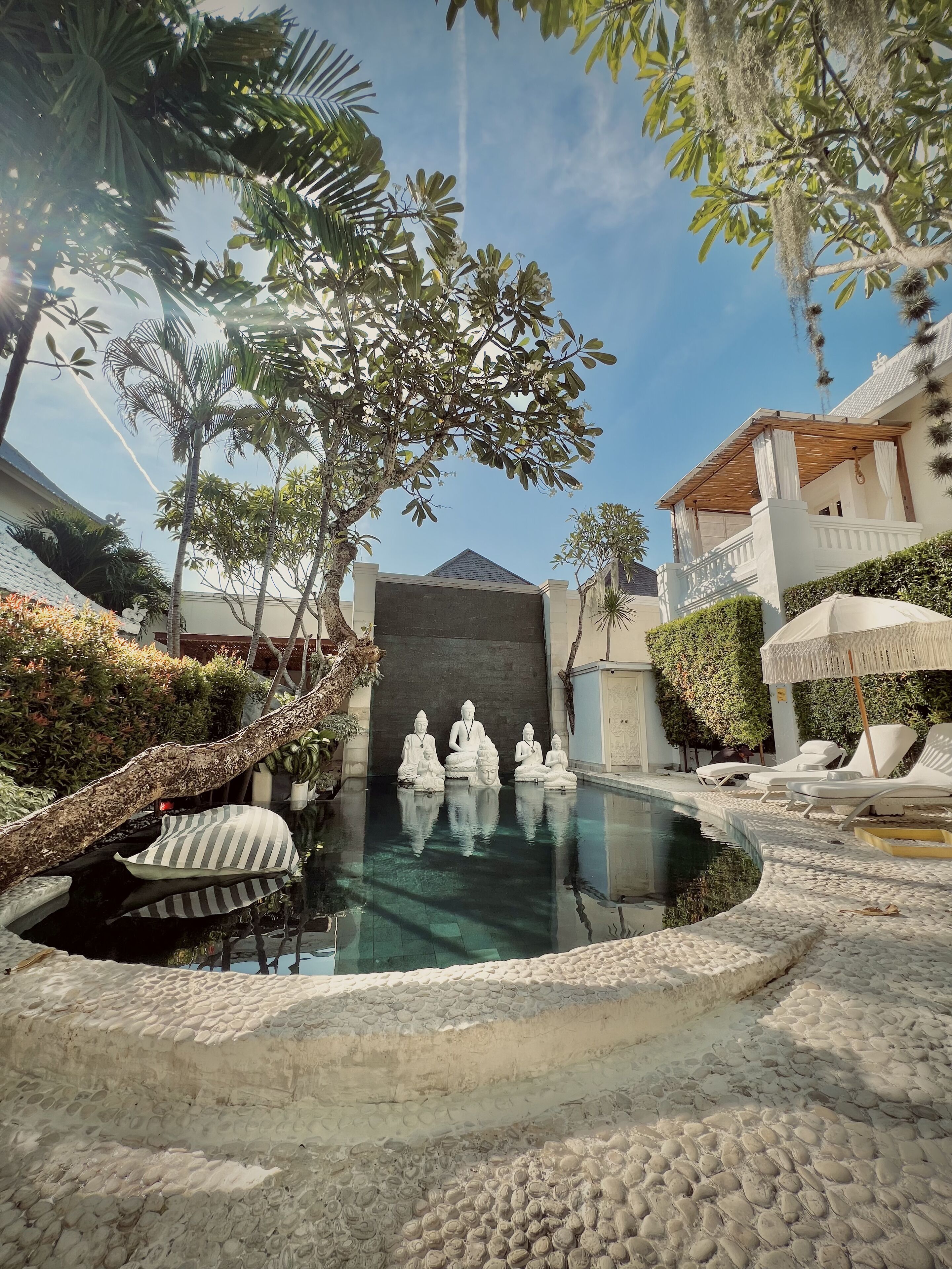 Un área de piscina tranquila con estatuas de Buda, rodeada de exuberante vegetación y un cielo despejado.