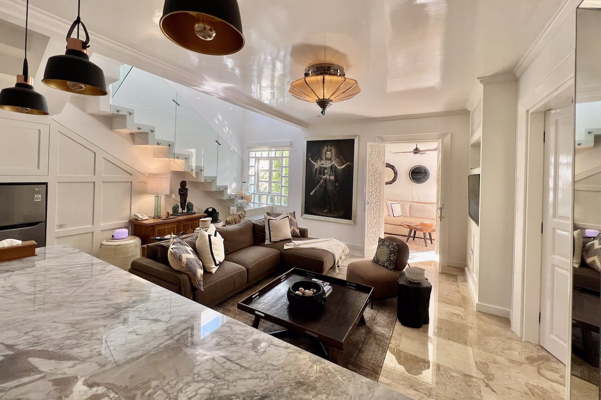 A spacious living area with a marble floor, a brown sofa, a coffee table, and a staircase leading to upper floors.