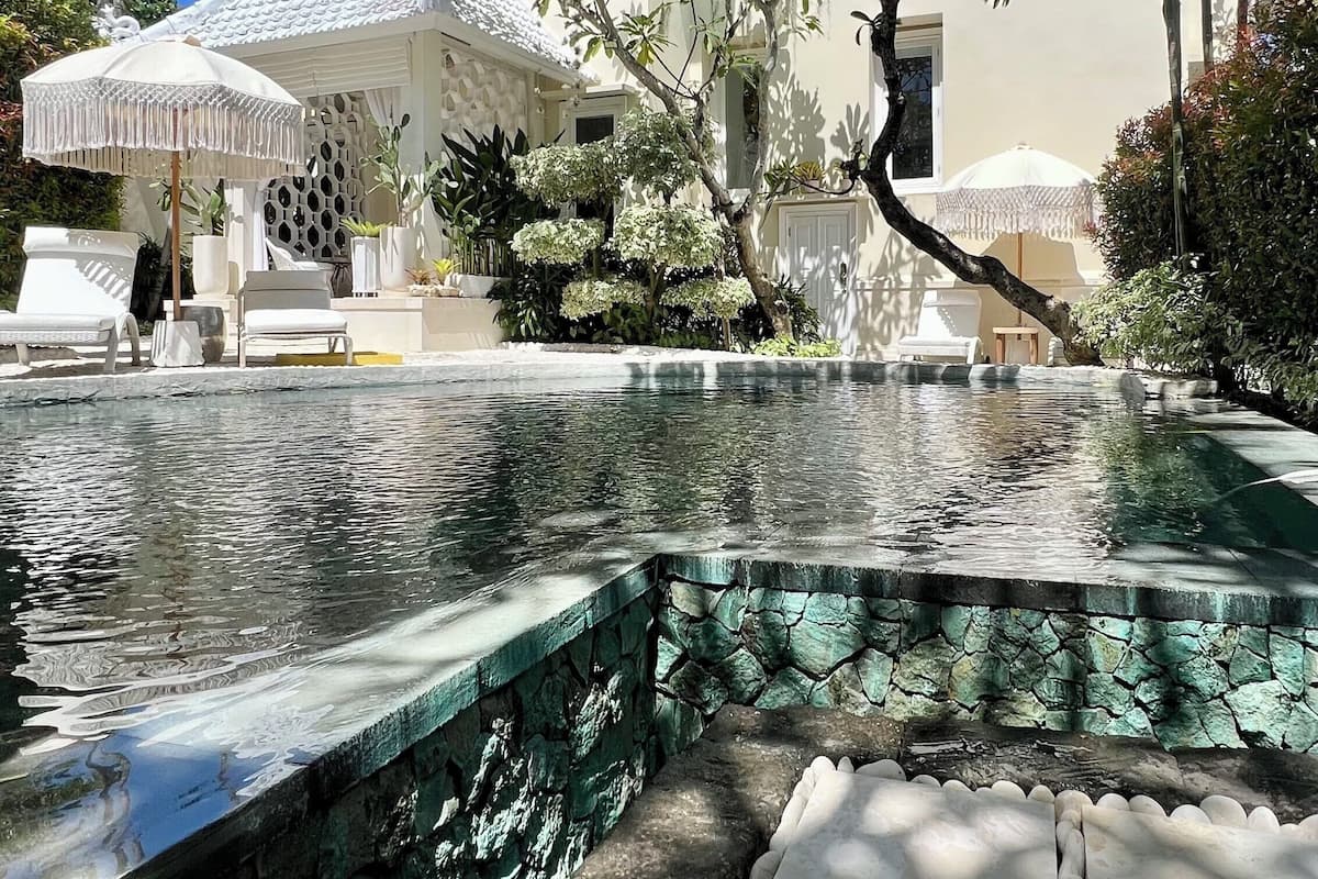 A pool area with a stone border, lounge chairs, and umbrellas.