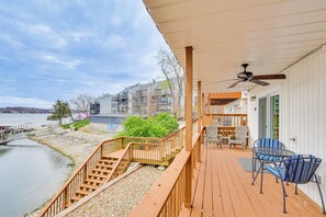 A wooden deck with a view of a lake, outdoor seating, and a staircase leading to a building. - Waterfront Condo w/ Deck on Lake of the Ozarks! (Lake Ozark)