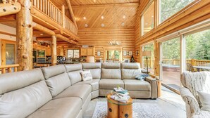 A spacious living room with a large L-shaped sectional sofa, a glass coffee table, and a wooden accent wall. - Mountain Cabin w/ Hot Tub: 4 Mi to Shaver Lake! (Shaver Lake)