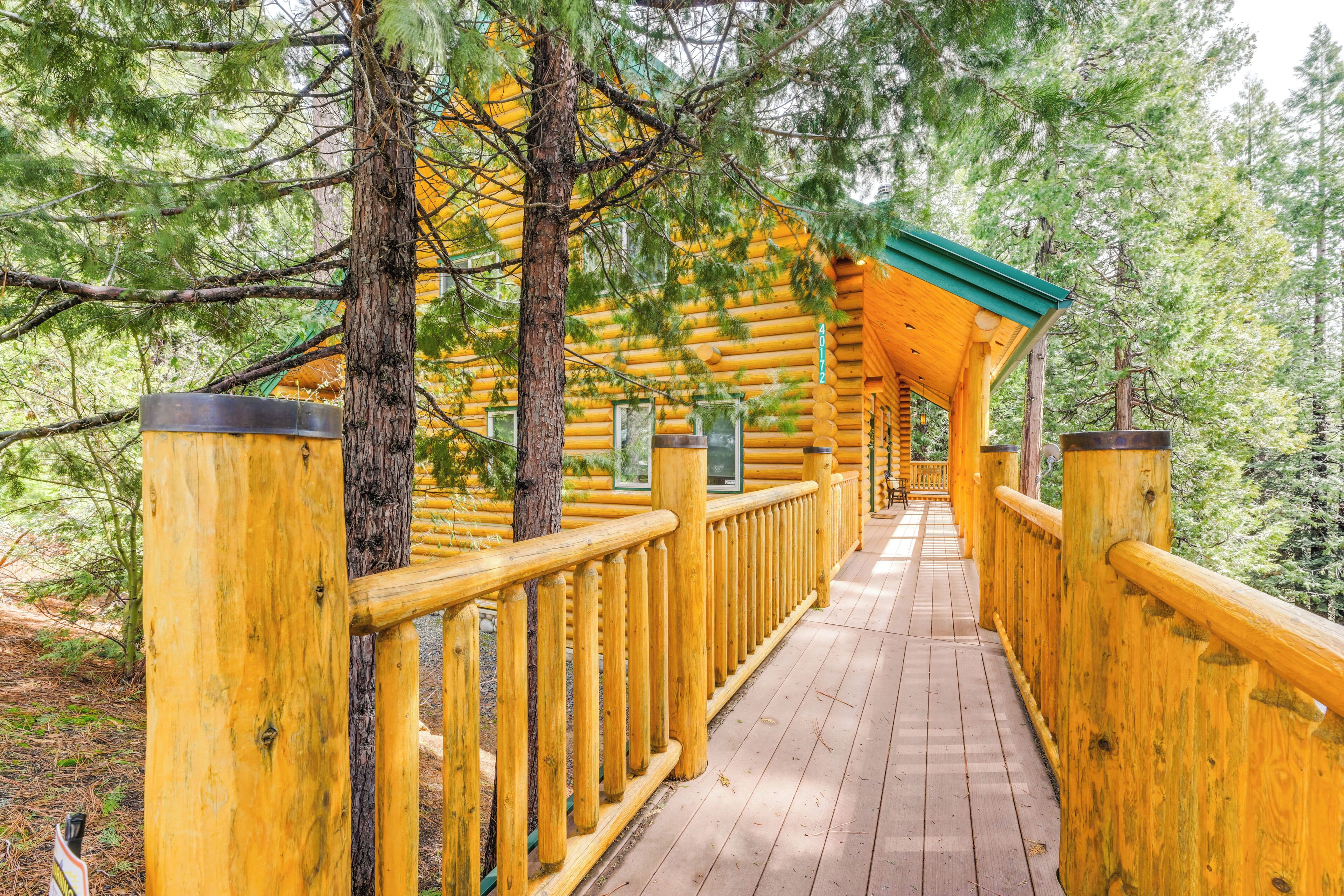 A log cabin with a wooden deck and a green roof, surrounded by trees.