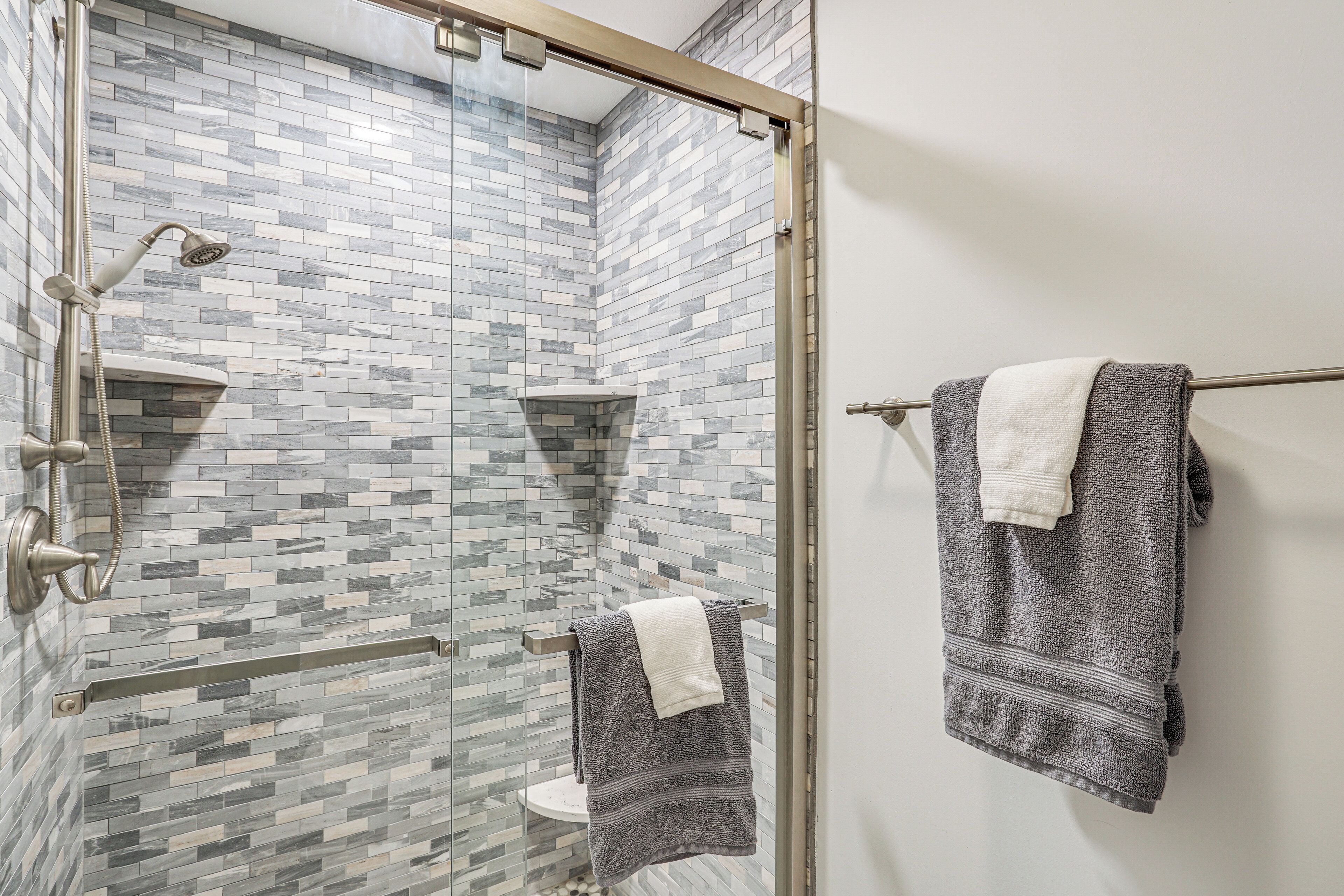 A shower with a glass door, a towel rack with two towels, and a tiled wall.