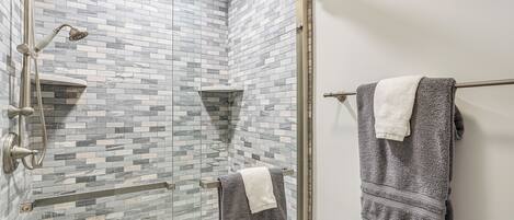 A shower with a glass door, a towel rack with two towels, and a tiled wall.