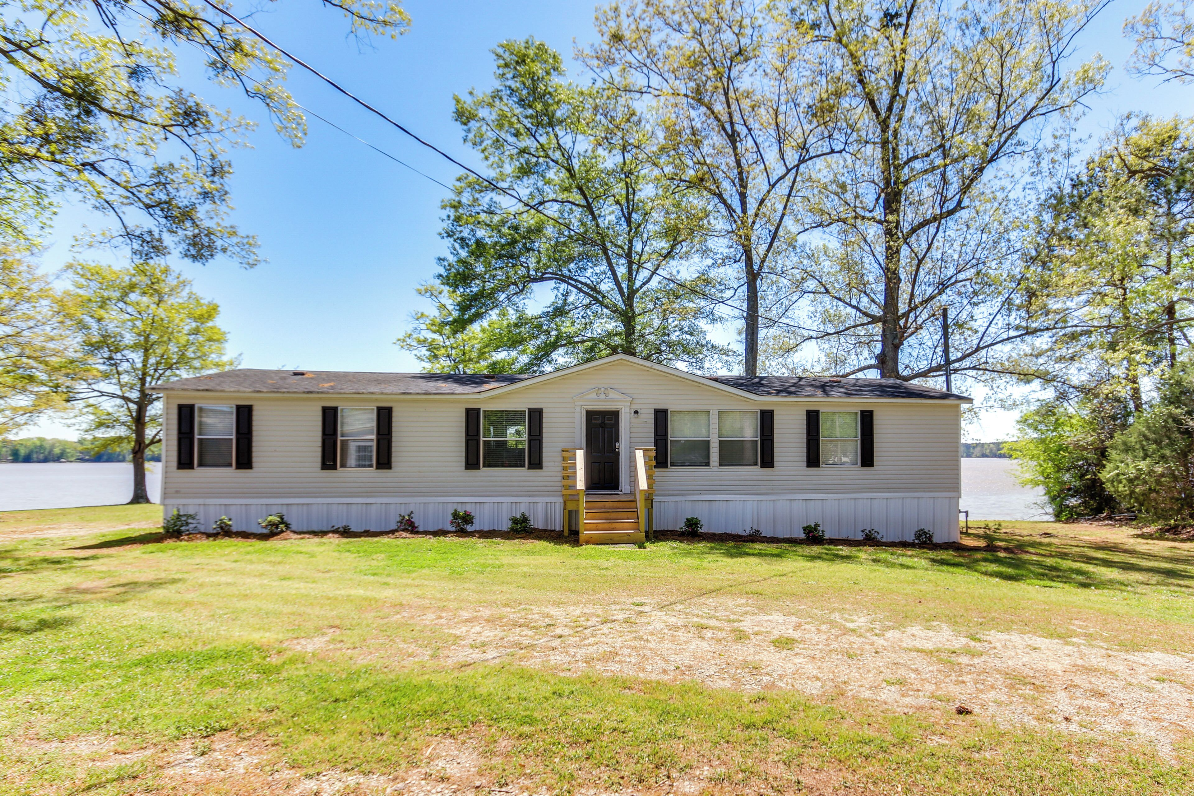A single-story house with a front porch, a small front yard, and a lake in the background.