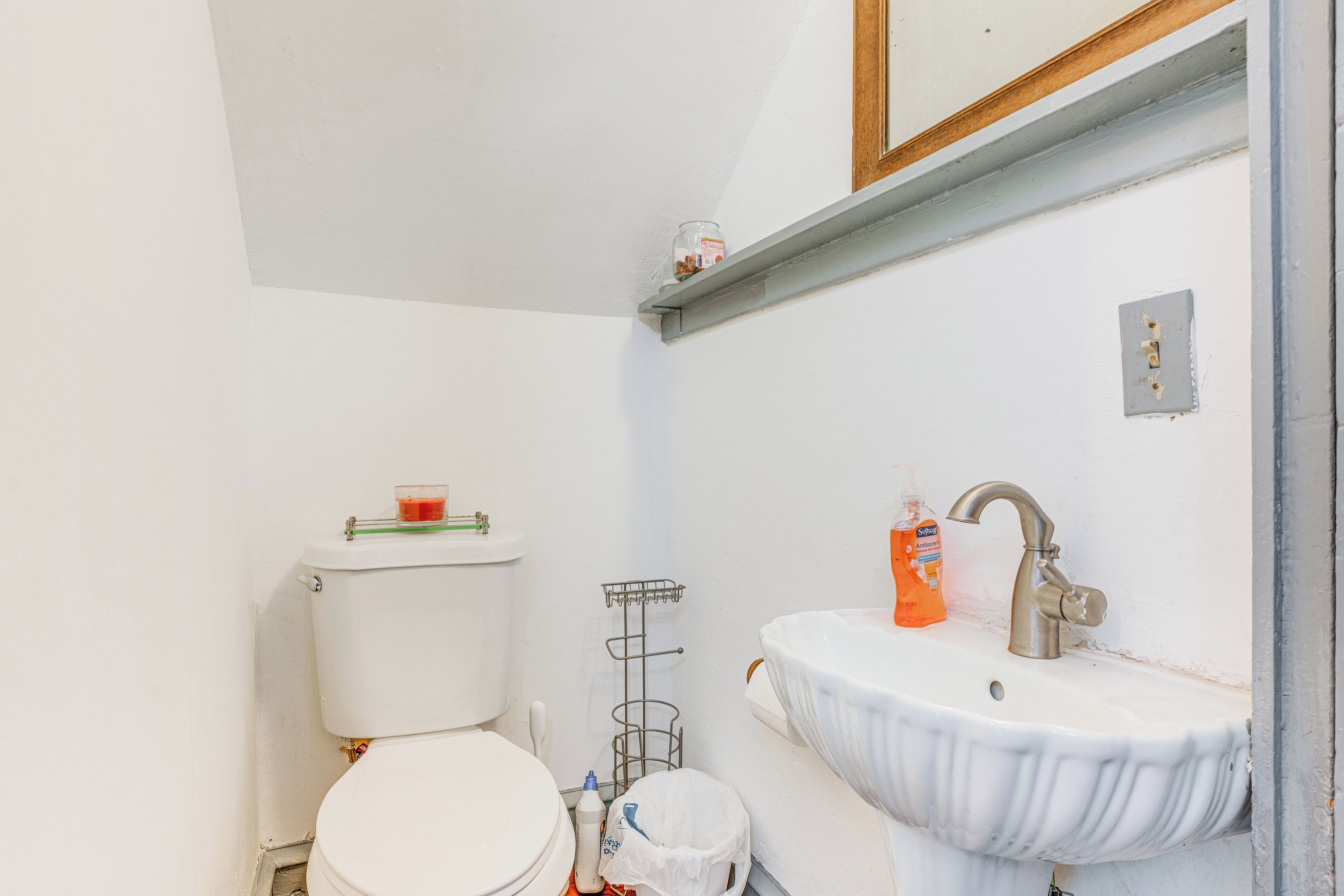 A bathroom with a toilet, sink, and a small shelf above the sink.