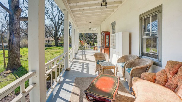 A covered porch with wicker furniture, a wooden table, and a view of the yard. - Experience a 17th-century Spring Manor (Norristown)