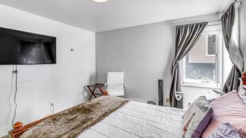 A bedroom with a bed, a TV mounted on the wall, a window with curtains, and a radiator.