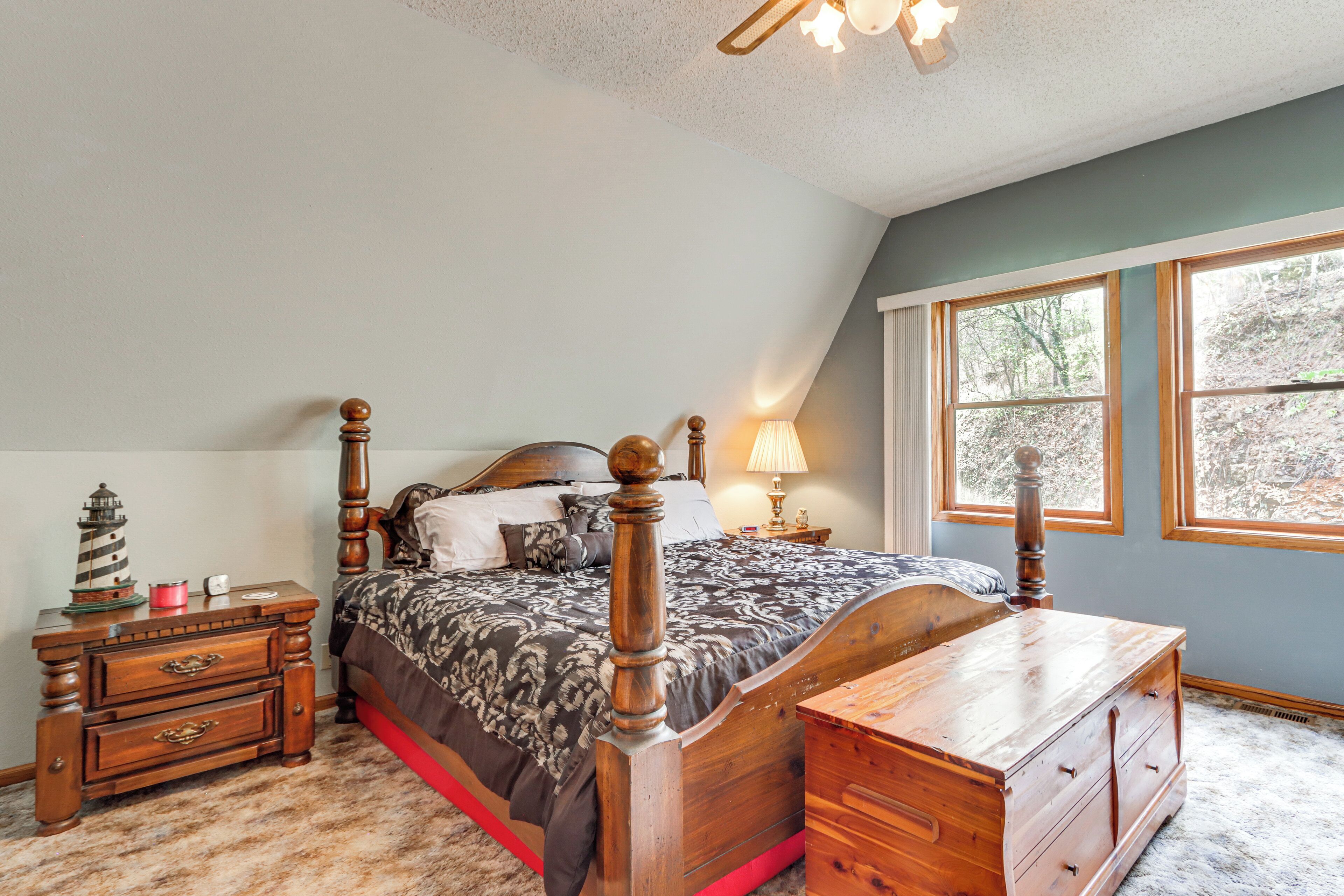 A bedroom with a wooden bed, a nightstand, a dresser, and a window with a view of trees.
