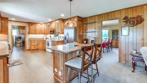 A spacious kitchen with wooden cabinets, a central island, and a dining area with chairs. - Spacious Mount Pleasant Home w/ Grill & Yard! (Mount Pleasant)
