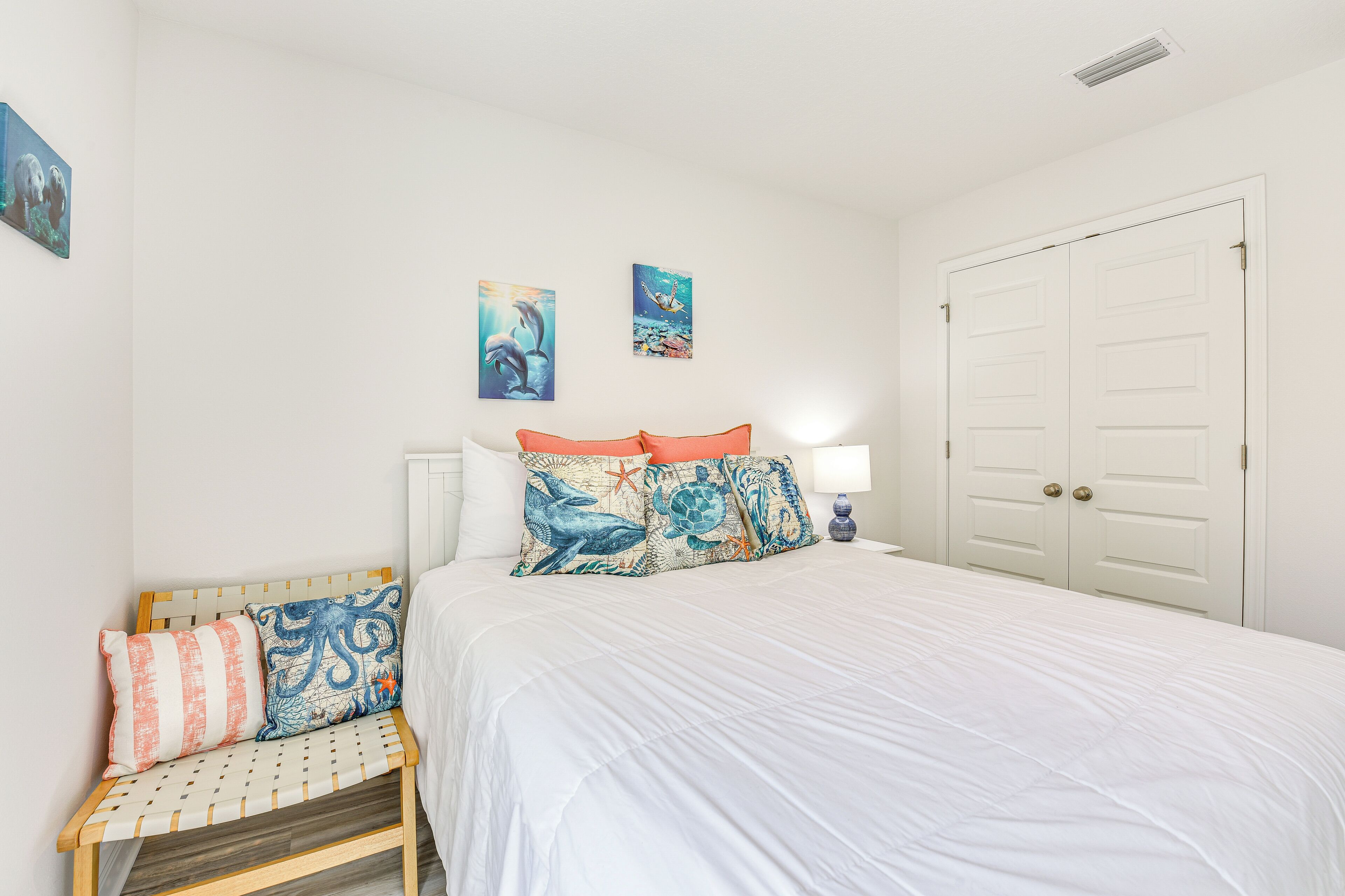 A bedroom with a large bed, a bench with cushions, and two wall art pieces.