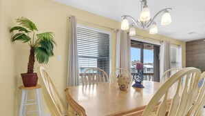 A dining area with a wooden table, white chairs, a potted plant, and a vase. - Sugar Dunes 124 | 🌅 Sound Views | 🌴 Steps to Beach | 🍽 Walk to Dining (Navarre Beach)