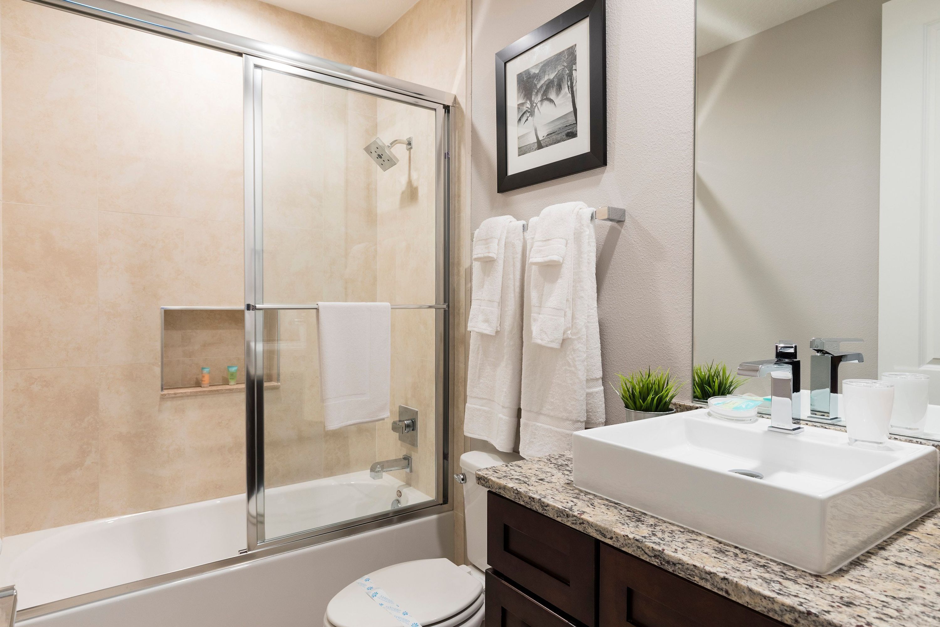 A modern bathroom with a glass-enclosed shower, a white toilet, a sink with a marble countertop, and a framed picture on the wall.