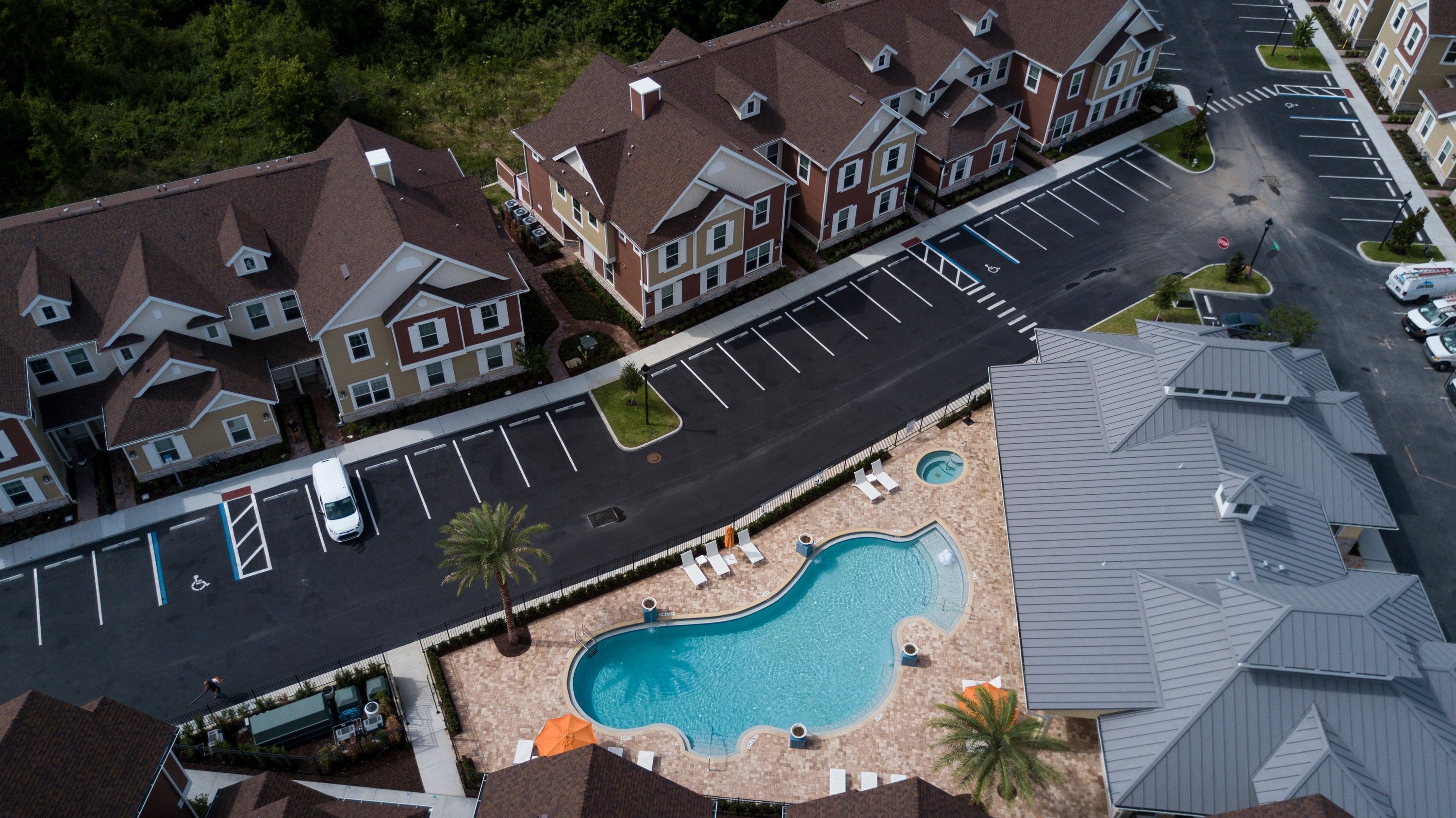 An aerial view of a residential area with a swimming pool, parking spaces, and houses with distinct architectural styles.
