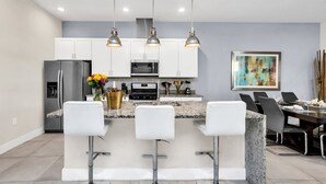 A modern kitchen with white cabinets, a granite countertop, and three bar stools. - 5 BR 6 BA Villa 5min Disneyworld Hot Tub BBQ (Kissimmee)