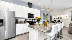 A modern kitchen with white cabinets, stainless steel appliances, granite countertops, and pendant lighting. - 5 BR 6 BA Villa 5min Disneyworld Hot Tub BBQ (Kissimmee)