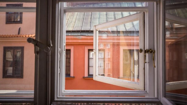 A window with a view of a building with a red facade and a metal roof.