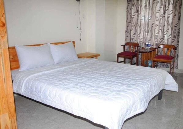 A single-bed room with a wooden headboard, a bedside table, a chair, and a small table with a bottle and a cup. - Hostel 15A (Da Nang)