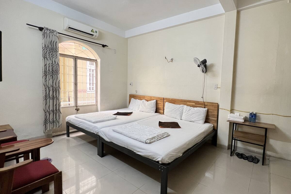 A clean, well-lit hotel room with a large bed, a small table with a water bottle, and a bench.