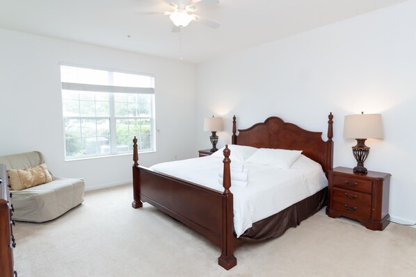 A bedroom with a large bed, two bedside tables with lamps, a window, and a chair.