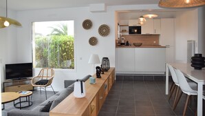 A modern living space with a sofa, a wooden coffee table, a TV, and a dining area with a table and chairs. - Superbe Maison Entièrement Rénovée 2024, Lumineuse à 400 m de la Plage (Sarzeau)