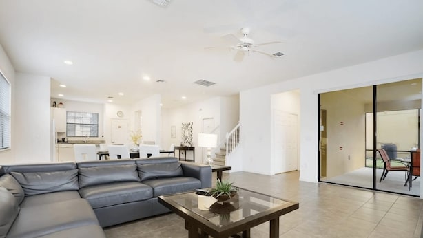A modern living room with a sectional sofa, a glass coffee table, and a kitchen in the background. - Grand Superior 4BD Pool Home at Disney Universal (Davenport)